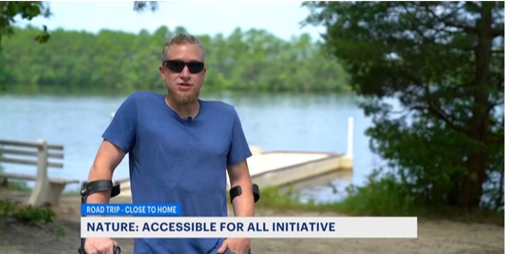Image of man in blue shirt and glasses talking in front of a lake