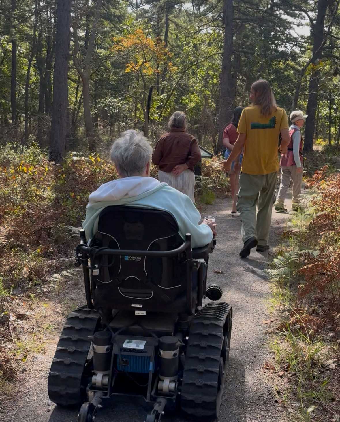 Group of people walking in woods, one using a power wheelchair