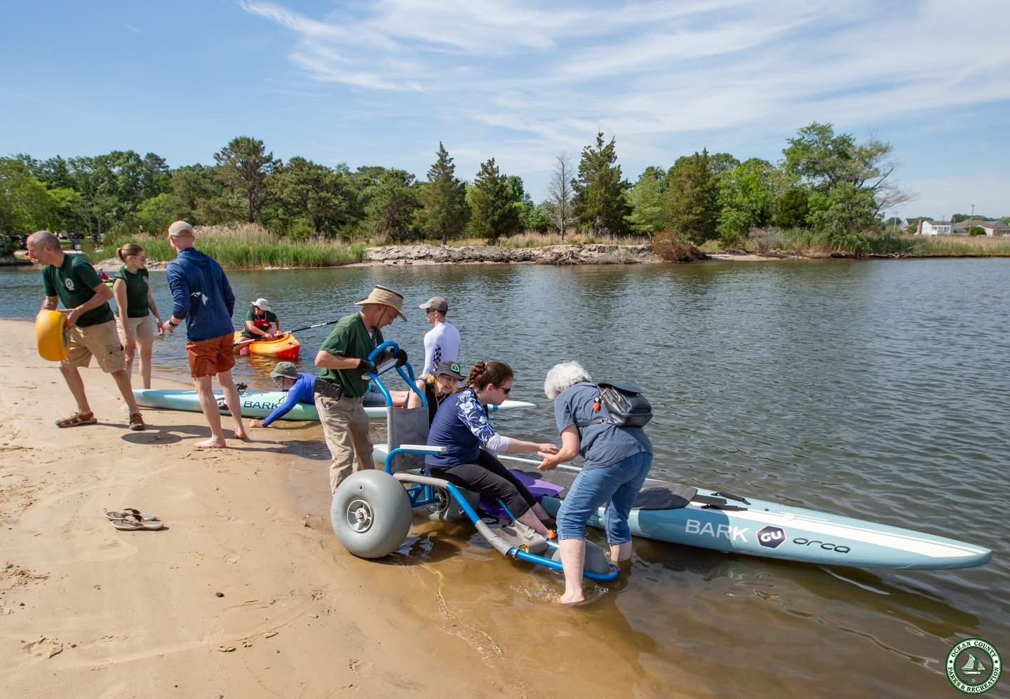 Lake with kayaks and people assisting others with mobility concerns